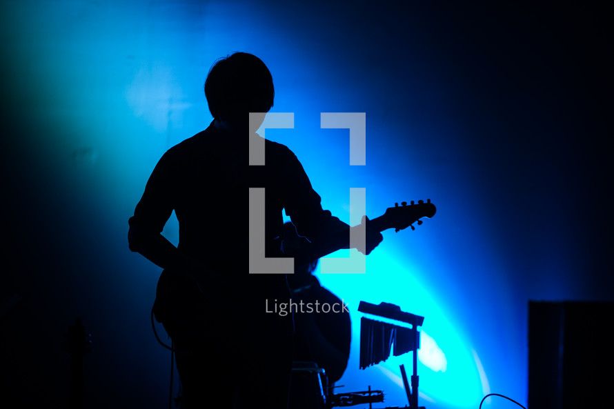 silhouette of a man on stage playing a guitar 