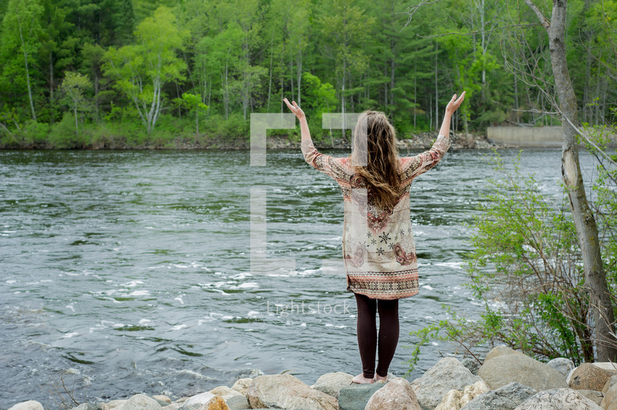 woman with her hands raised in worship at a river