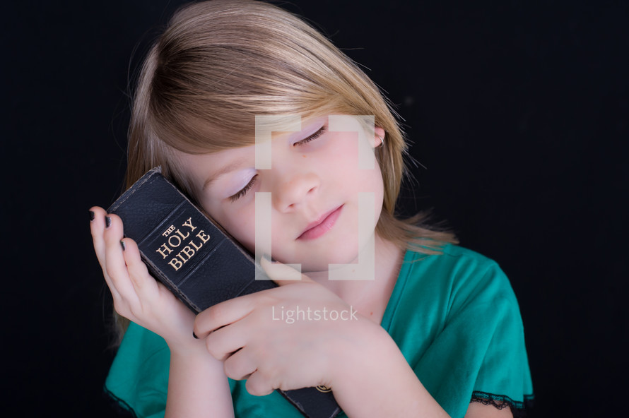 A child resting her head on a Bible 