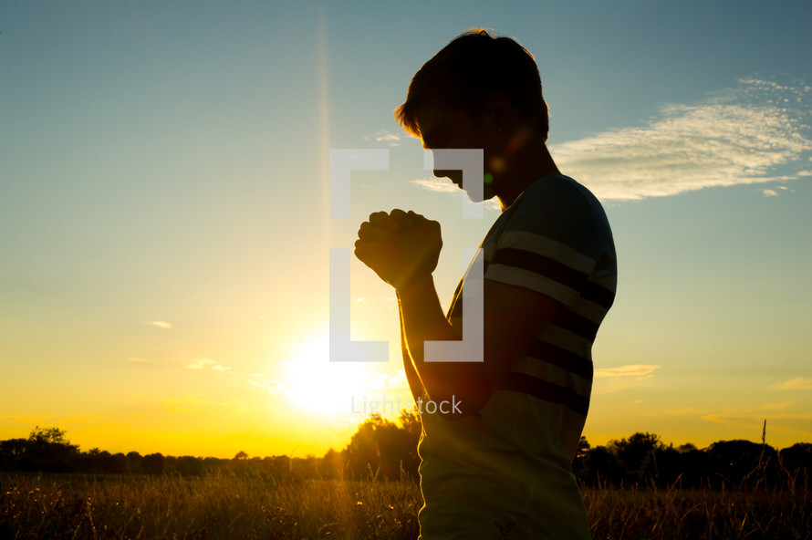 silhouette of a man with praying hands at sunset 