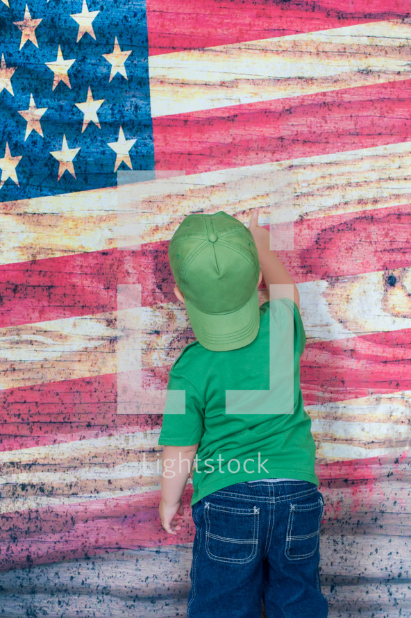 toddler boy pointing to an American flag painted on a wall 