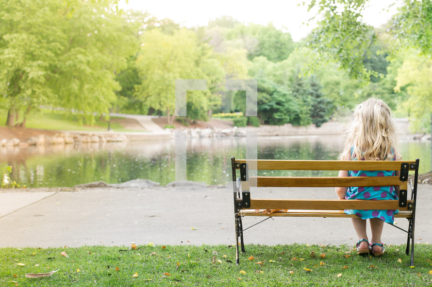 woman sitting on a park bench looking out at a lake 