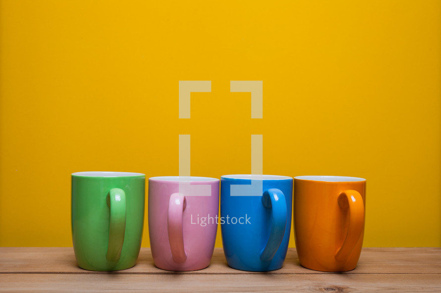 a row of colorful coffee mugs against a yellow wall 