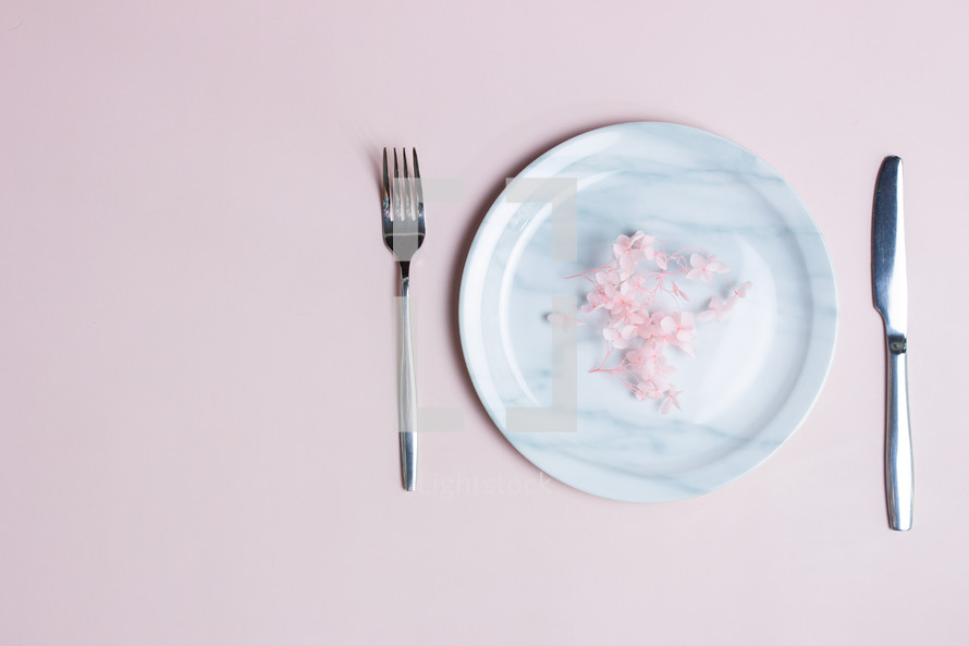 Sweet diet concept with marble plate, knife and fork over the pink background. 