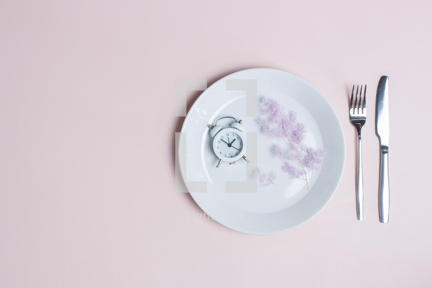 Eating healthy concept with clock, knife and fork over the pink background.