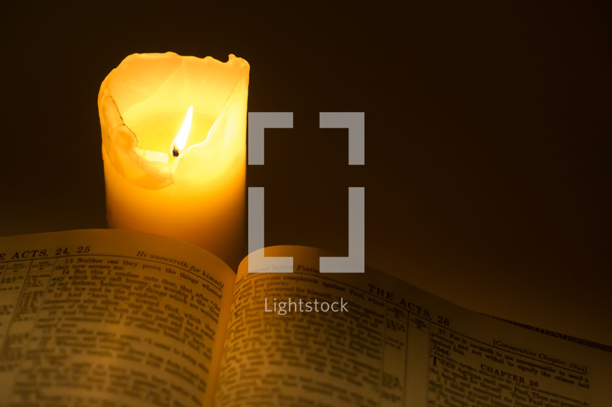 Lit candle burning next to a Bible open to the Book of Acts.