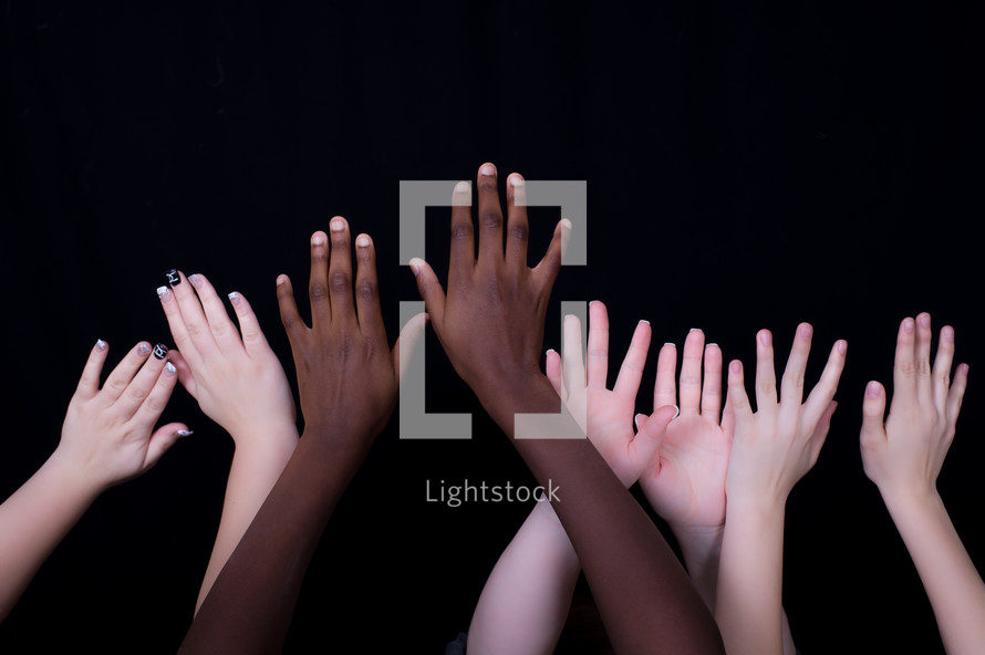 Children's hands raised in the air against a black background 