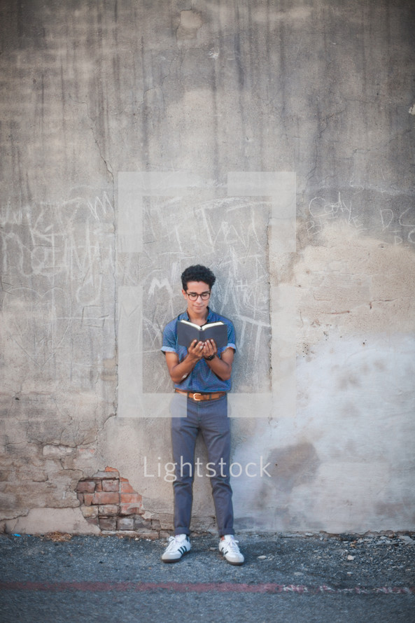 man reading a Bible standing in front of a wall with graffiti 