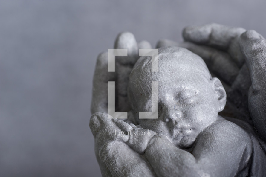 Sculpture of hands holding a newborn baby.