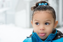 a toddler girl sticking out her tongue to catch snow flakes 