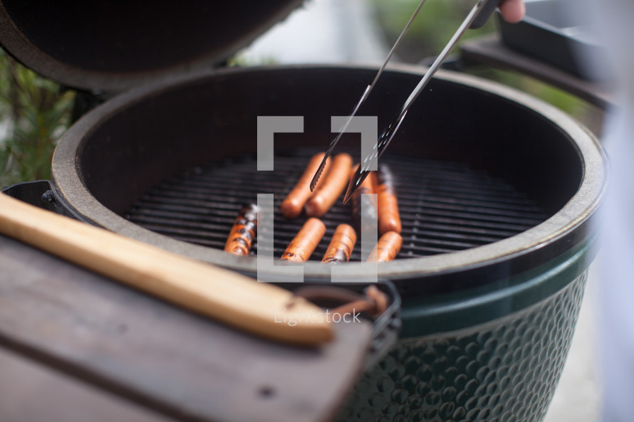 turning hotdogs on a grill 