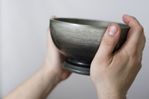 Hands holding pewter bowl.