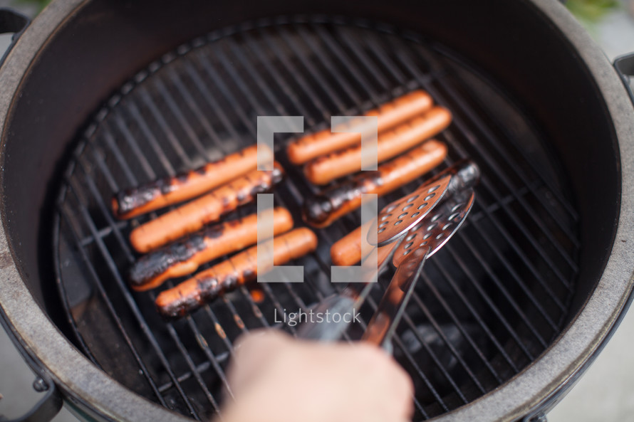 flipping hotdogs on a grill 