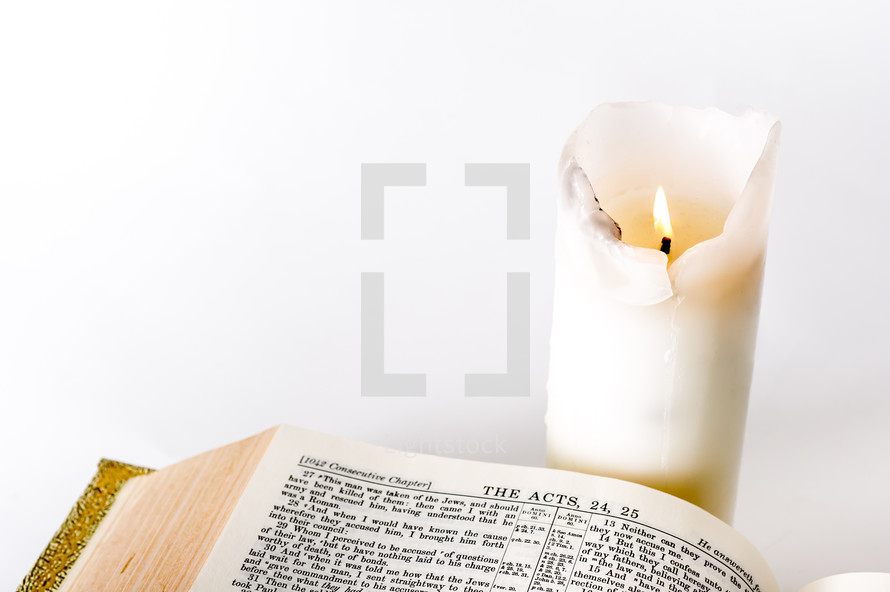 Lit candle burning by a Bible open to the Book of Acts.