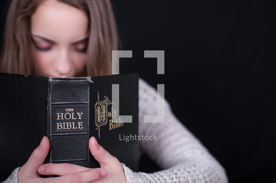 Teen girl praying while holding an open Bible.