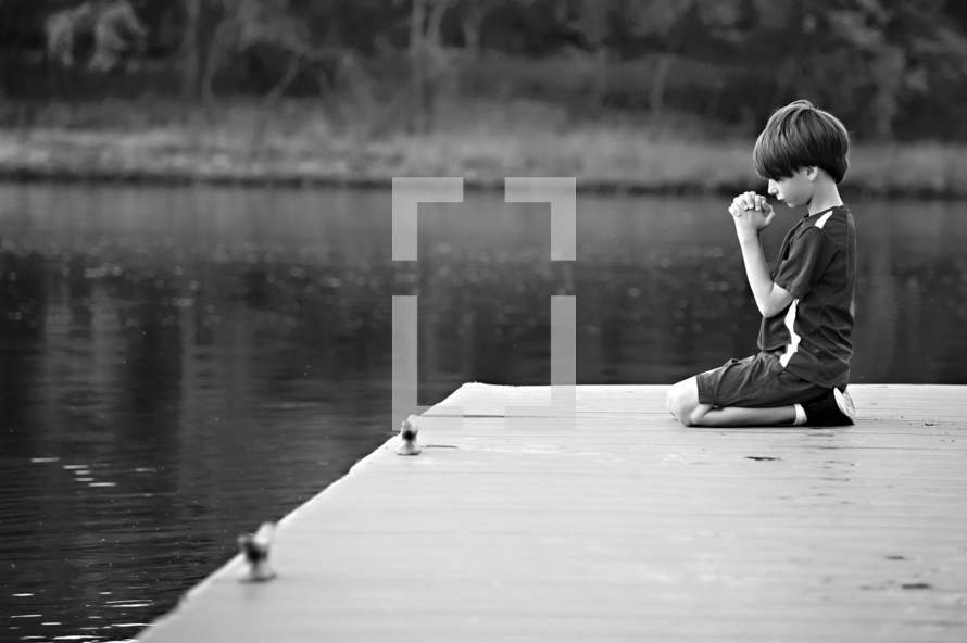 boy child kneeling in prayer on a dock 