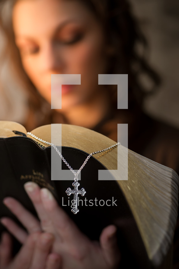 woman reading a Bible and a cross necklace bookmark