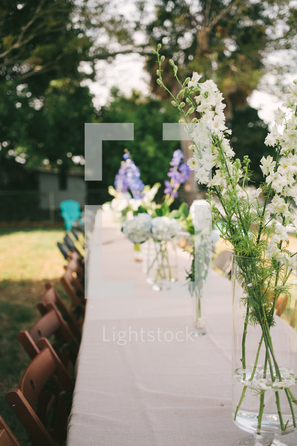 row of flowers in vases on a table at a wedding reception