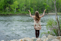woman with her hands raised in worship at a river