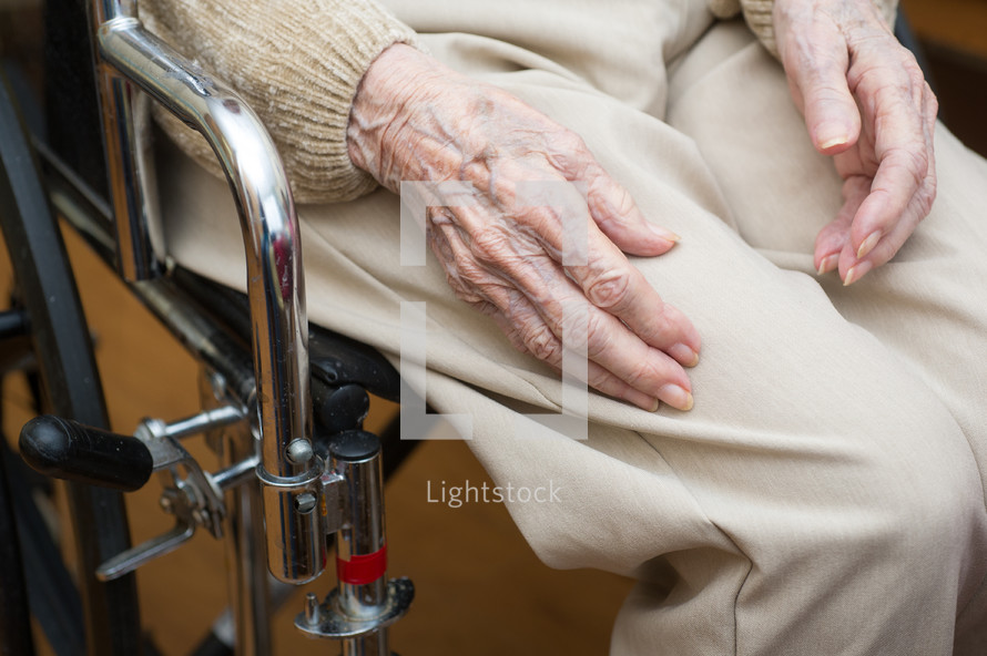 Hands of an elderly person sitting in a wheelchair.