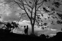 a couple hugging standing under a tree 