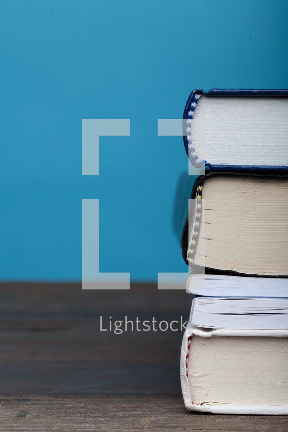 A stack of books on a wooden surface with a blue background.