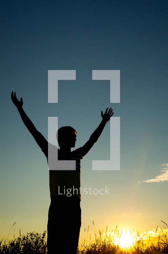 silhouette of a man with raised hands in worship at sunset 
