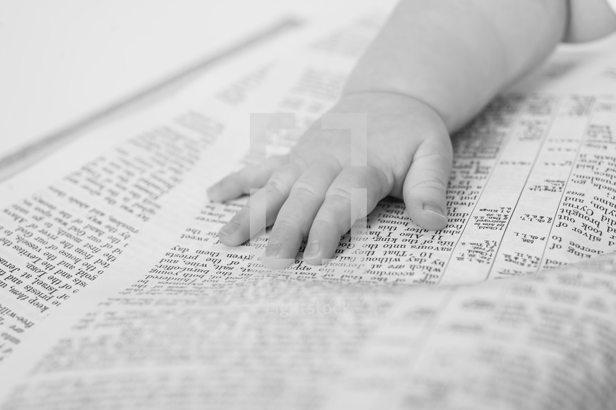 An infant's hand laying on an open bible