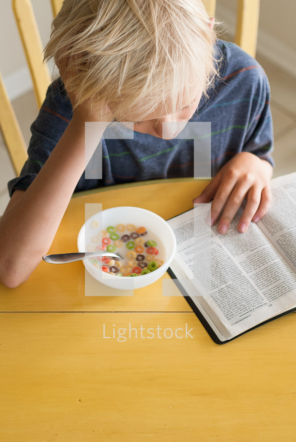 morning devotional, boy child reading a Bible while eating milk and cereal 