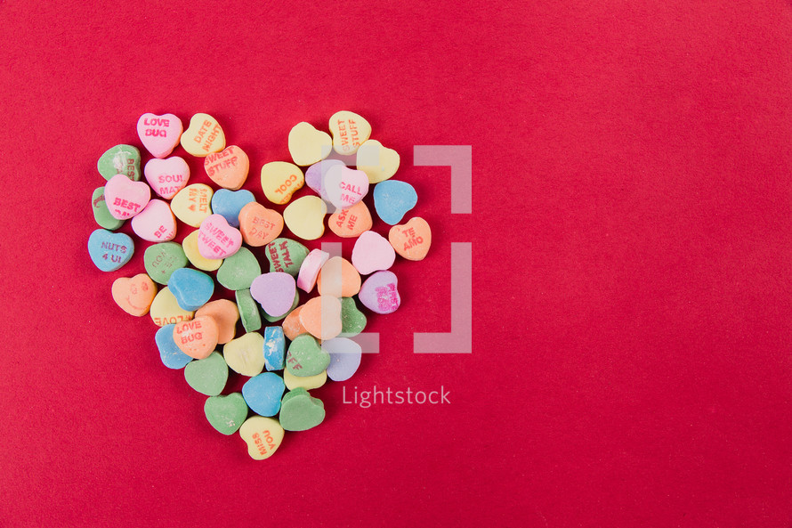 conversation hearts spilled in the shape of a heart on a red background 