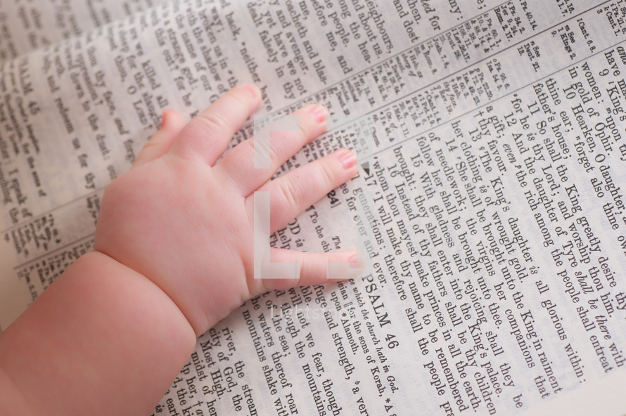Close-up of infants hand laying on a bible opened to Psalm 46