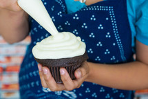 woman icing a chocolate cupcake 