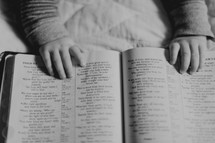 infant's hands on the pages of a Bible 