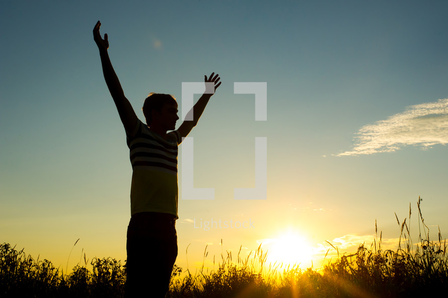silhouette of a man with raised hands at sunset 