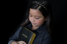 A young girl holding a Bible close to her heart 