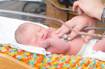 newborn baby with a stethoscope being pressed to its chest.