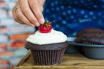 woman adding a strawberry to a chocolate cupcake 