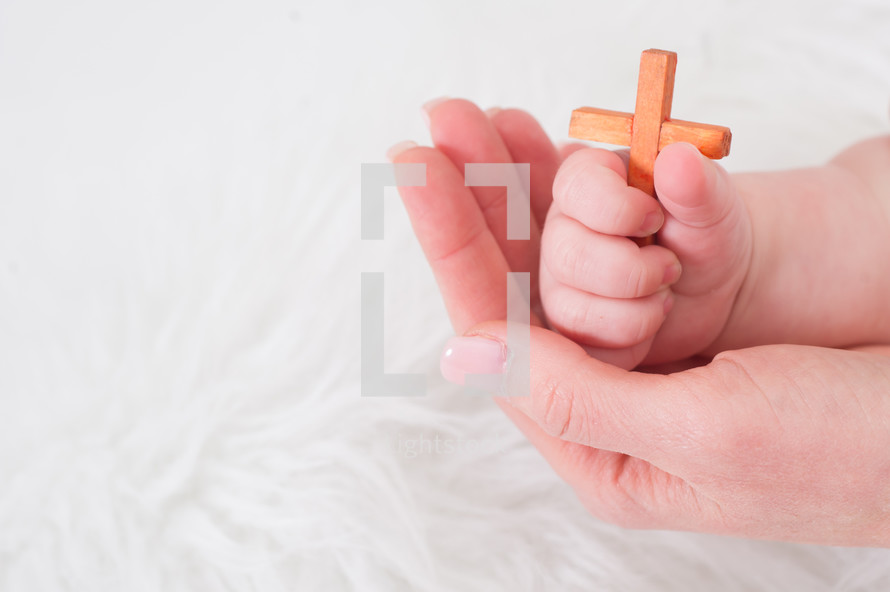 Infant holding a small wooden cross, a woman's hand cradling the infants