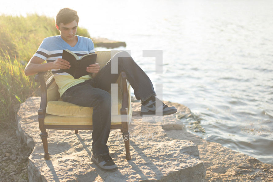 man reading the Santa Biblica in a chair on a beach 