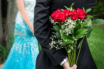 A man holding a bouquet of red roses behind his back for his date. 
