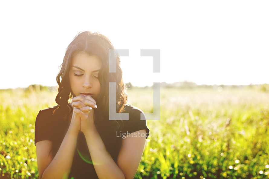 woman with praying hands in a field 