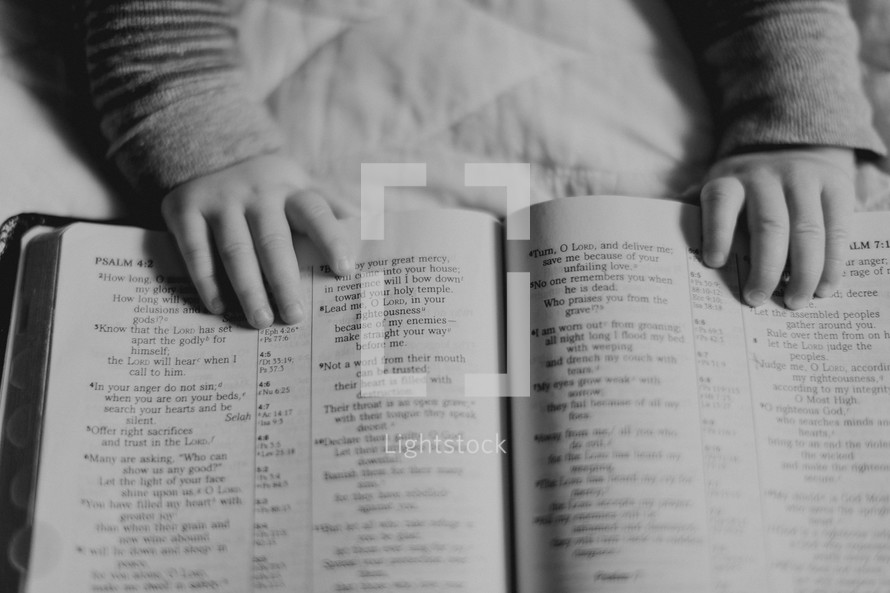 infant's hands on the pages of a Bible 