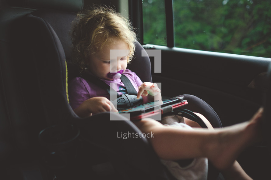 toddler with an iPad in a carseat 