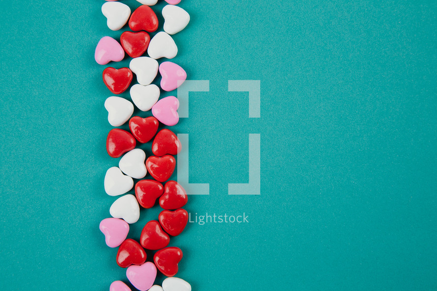 Small heart shaped candies lined up on an aqua background.