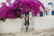 woman standing on a sidewalk under fuchsia flowers in Greece 