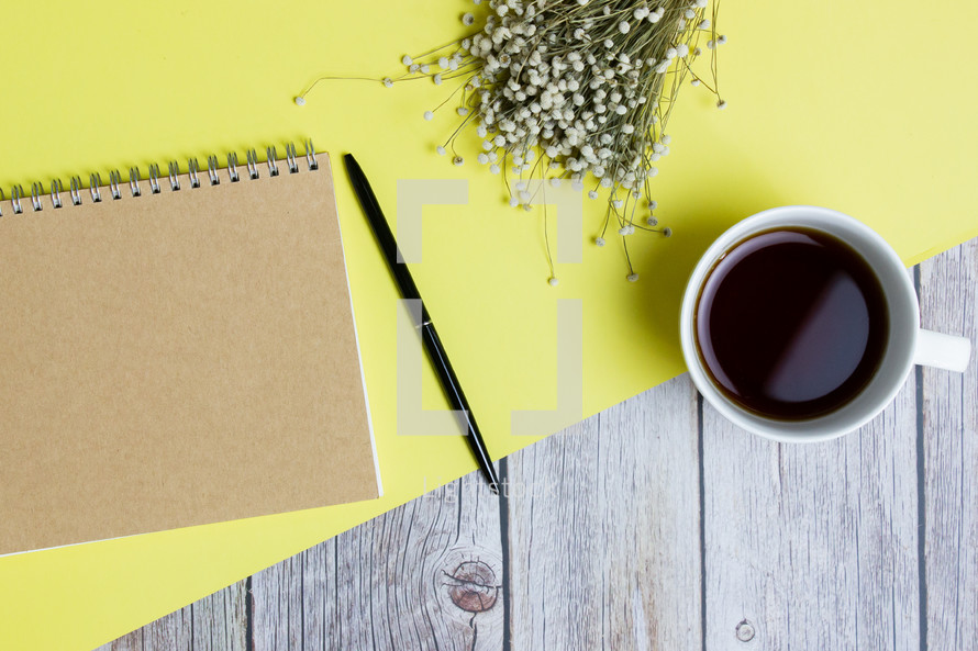 Fun colorful working items with notebook, pen, coffee cup and flowers over the yellow and wooden table. 