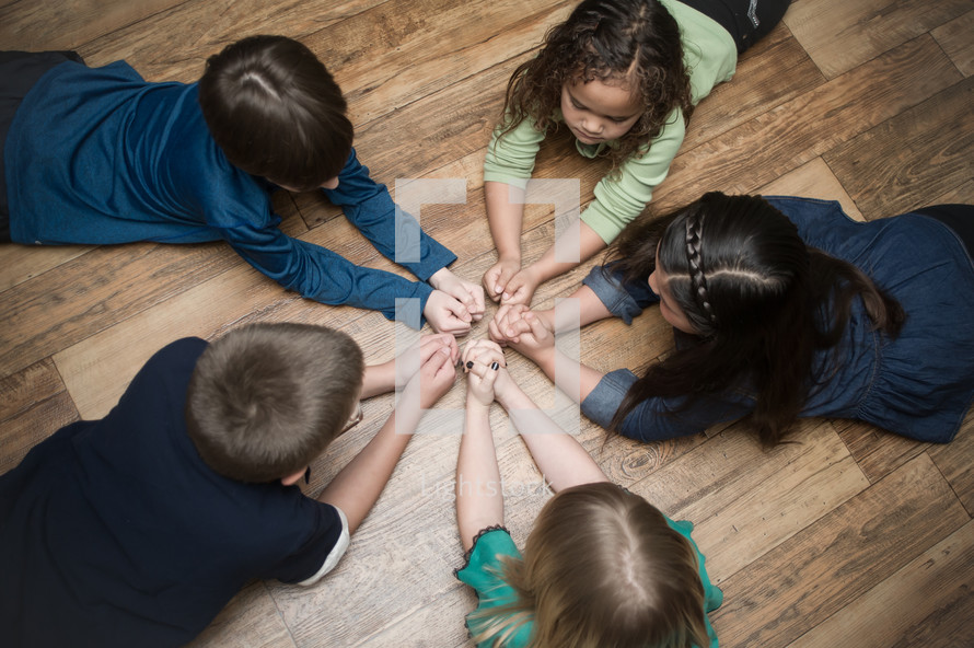 children with praying hands lying on the floor in a circle 
