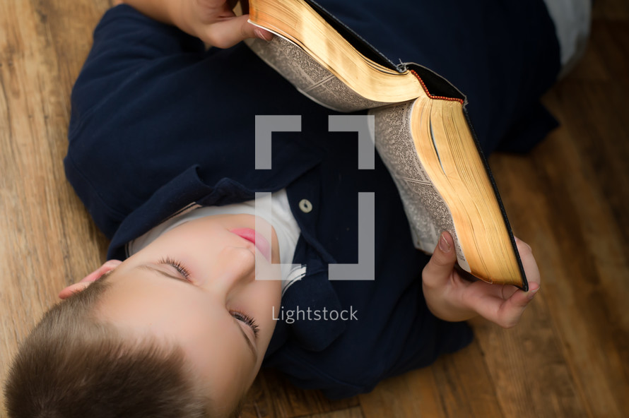 A boy reading a Bible lying on a floor 