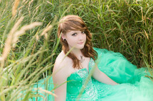 teen in a green prom dress sitting in a field 