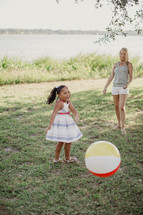 A little girl and woman laughing as they toss a beach ball.